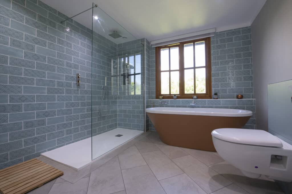 A bathroom with traditional decorative sea green tiles and a copper coloured free standing bath