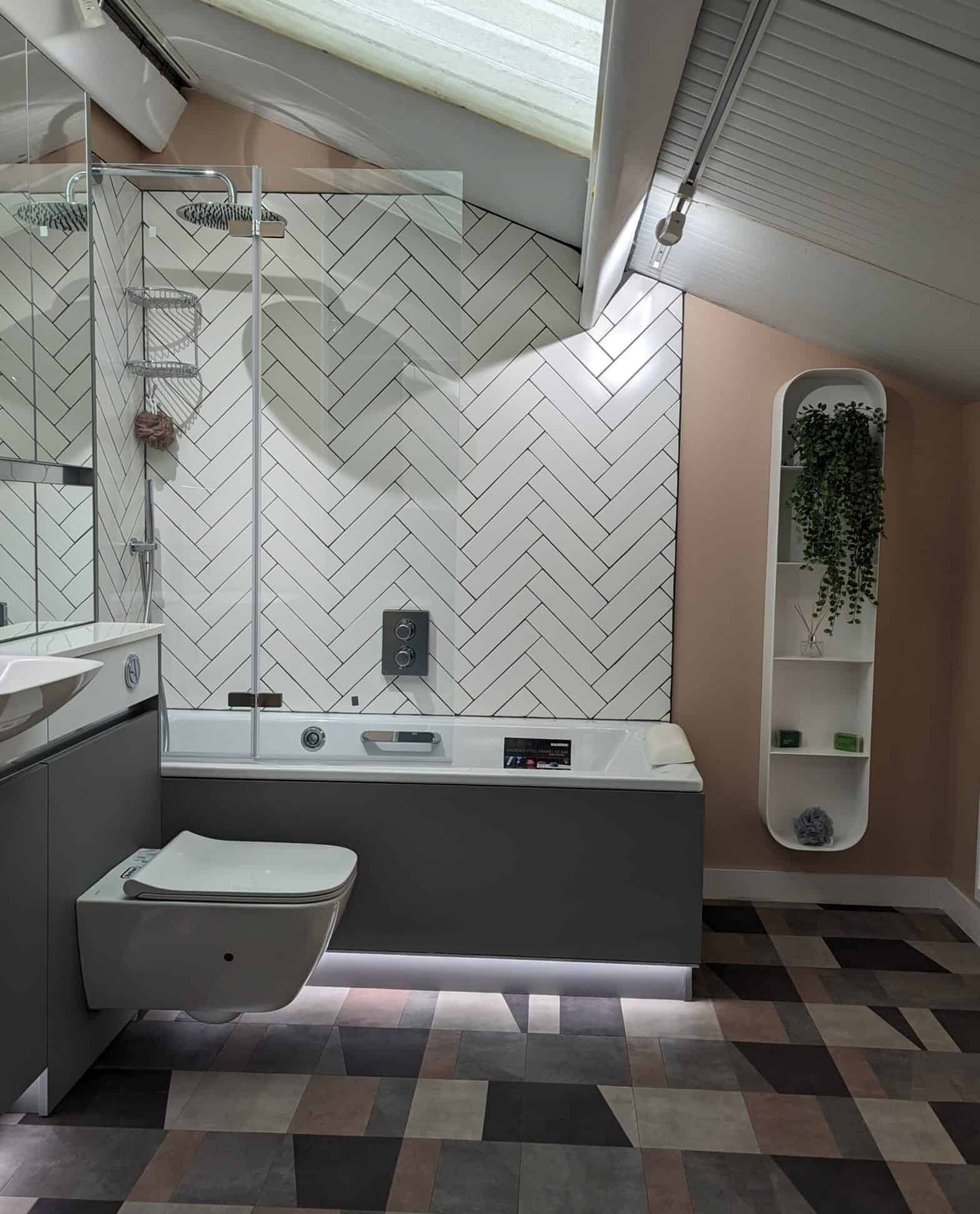 A bathroom with pink painted walls, white tiling in a herringbone pattern and a combination of grey and mirrored furniture.