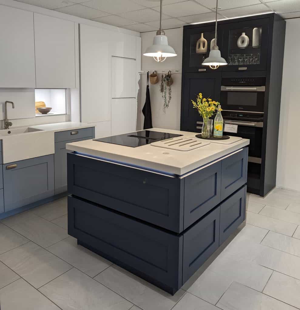 A picture of our modern shaker style kitchen, with cube island, in medium blue, oven stack in deep blue, with white worktop and wall units.