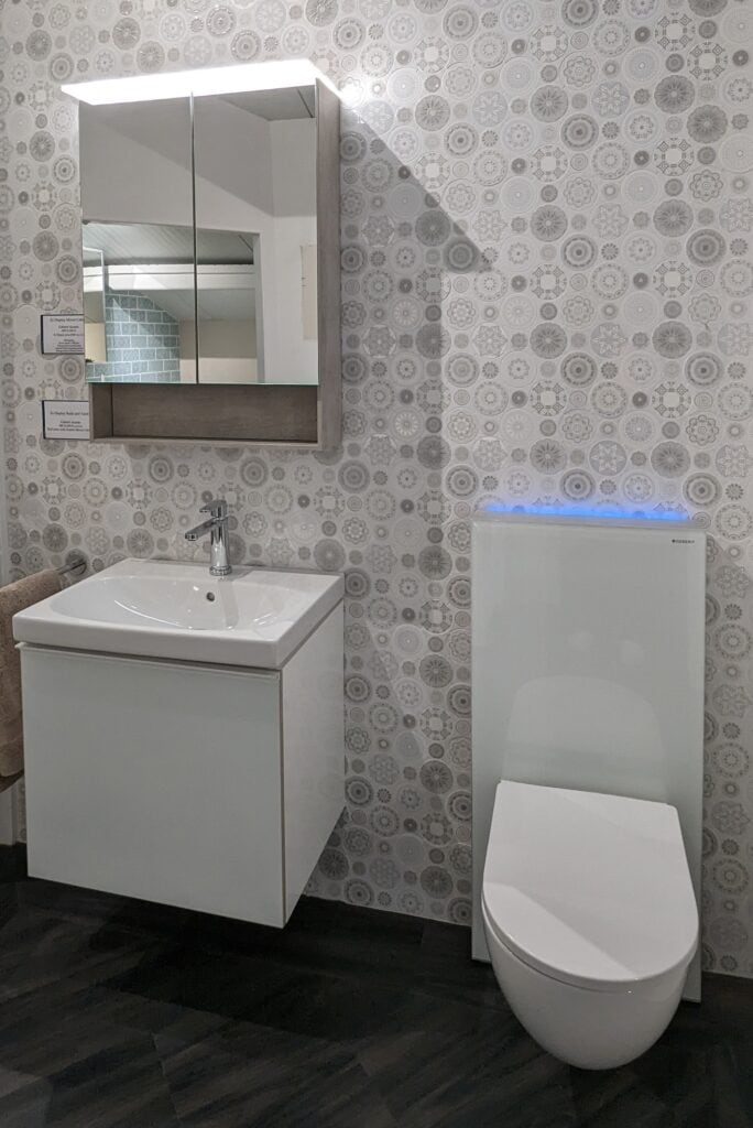 A corridor bathroom display with vanity unit, wall hung WC and neutral frosted look tiles