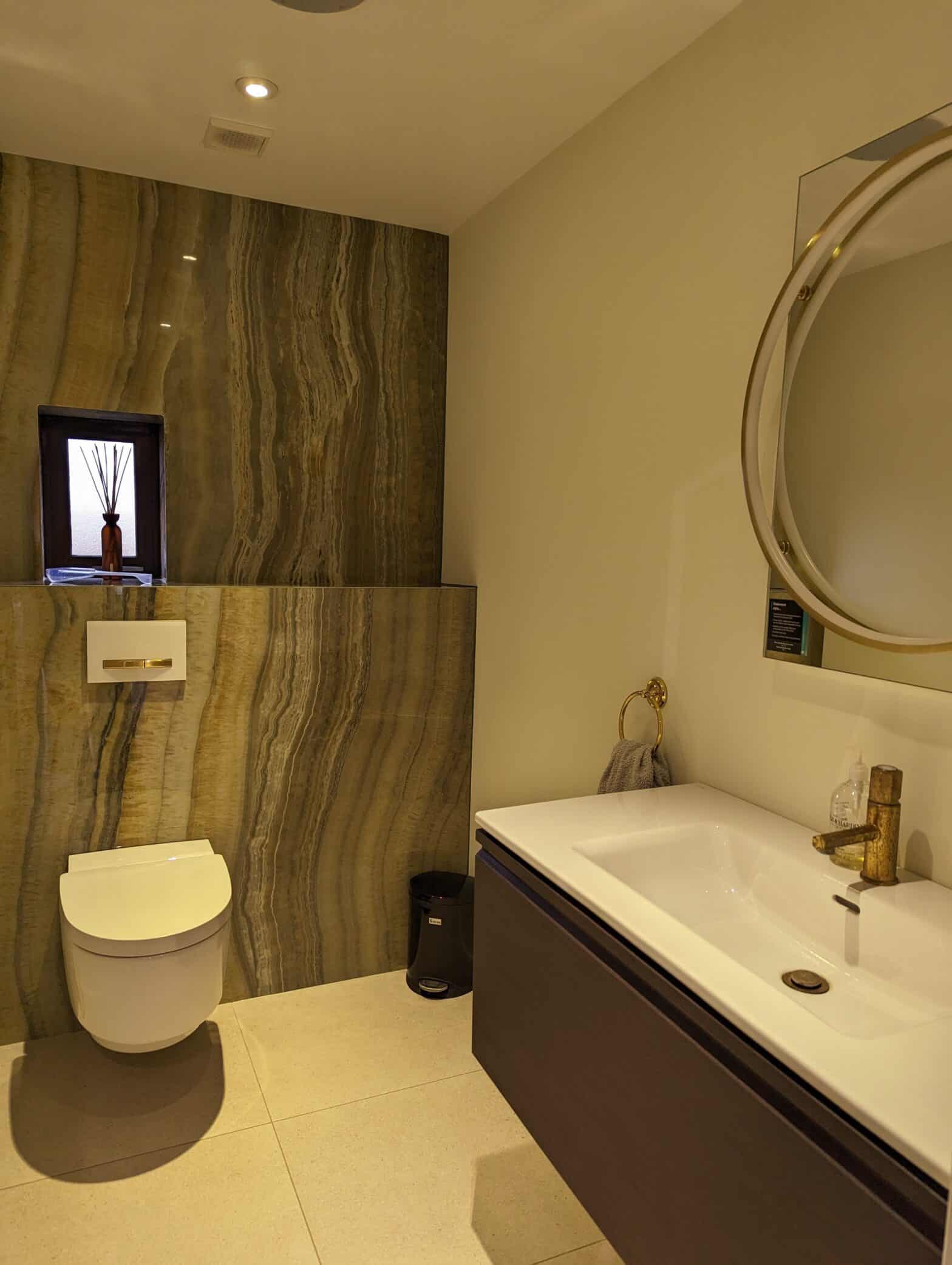 A photo of our customer WC featuring a large format stone tile showing an agate slice in green. A wall hung toilet from Gebrit sits on the same wall with a wall hung wide vanity to the right.